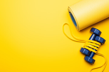 top view of fitness mat with blue dumbbells and resistance band on yellow background