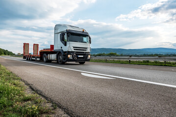 Fototapeta na wymiar Semi trailer transportation truck with empty trailer on a highway driving at bright sunny sunset. Transportation vehicle