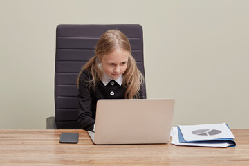 A cute blonde girl sits in a chair in the office and looks at a laptop.