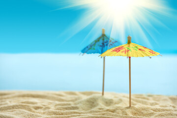 Sun umbrellas on sandy beach with blurry blue ocean,  sky and sun beams. Summer background. Soft focus