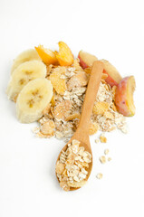 Vertical image.Wooden spoon, heap of oatmeal, corn flakes, pieces of banana, peach, plum on the white surface.Delicious ingredients for healthy breakfast