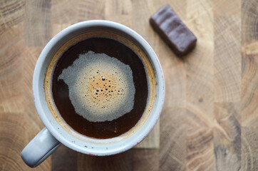 Close-up brewed coffee in a cup with candy on a wooden table. Coffee and chocolate candy on wooden background with copy space. Freshly brewed coffee in a vintage gray mug.