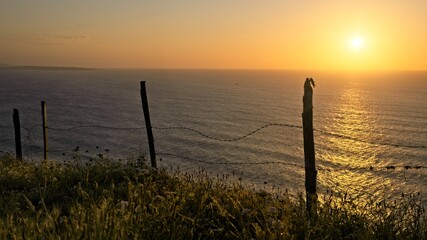 Obraz premium Barbed wire in front of the ocean at sunset 