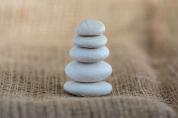Fototapeta na wymiar One simplicity stones cairn on jute brown background, group of five light gray pebbles built in tower