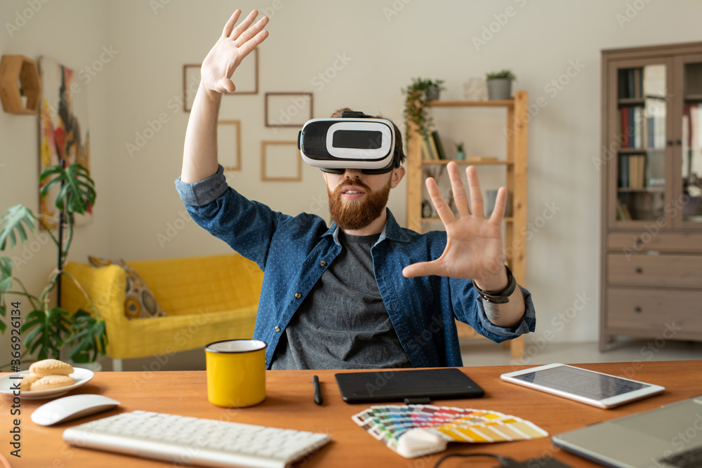 Wall mural content curious bearded man sitting at desk in home office and gesturing hands while testing new app