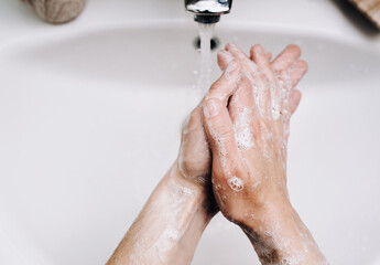 Fototapeta premium Female hands with soapy foam in a stream of tap water in the bathroom close up. The concept of hygiene, cleanliness and protection against coronavirus COVID-19.