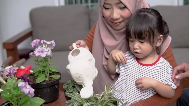 daughter sees her mother holding a watering can while watering plants on the terrace to take care of the plants
