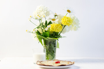 Pancakes decorated with red currant, milk glass flowers in vase on white background