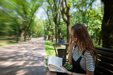 Obraz premium Charming red-haired teen girl in the Park reading a book on a bench