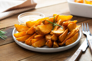 Fried potato chips with herbs and sauce in white plate, golden roasted potatoe slices with herbs.