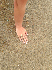 Female hand with blue nails on the background of sea sand