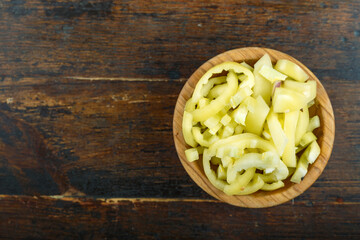 Sliced raw yellow peppers in a bowl on a wooden background. Vegetable, ingredient and staple food.