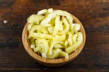 Sliced raw yellow peppers in a bowl on a wooden background. Vegetable, ingredient and staple food.