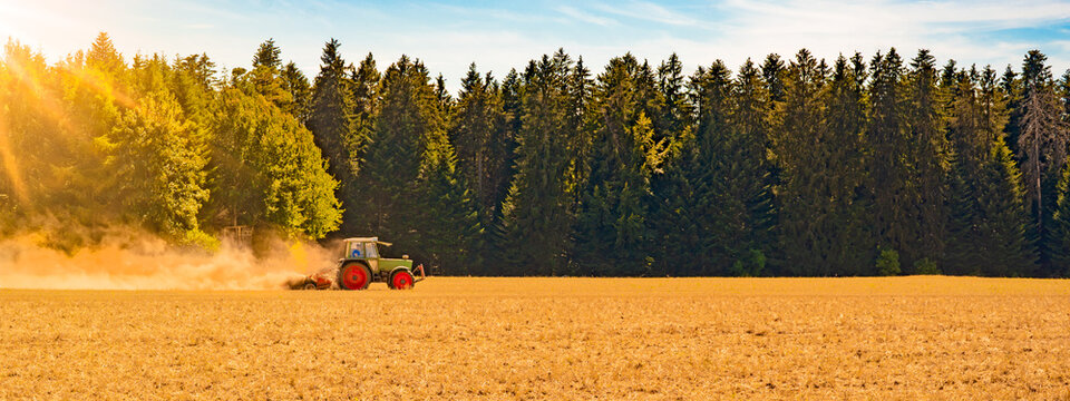 Sommer auf dem Land / Landwirtschaft Ernte Wald Hintergrund Banner Panorama: Alter Traktor beim Fr&auml;sen von Stroh Getreide Gersten Weizen Feld, mit aufgewirbeltem Staub, im Schwarzwald, Deutschland
