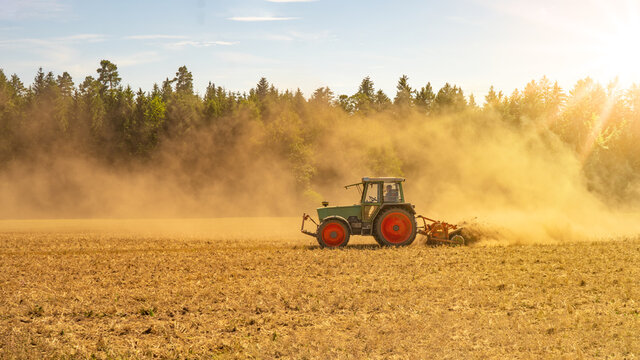 Sommer auf dem Land / Landwirtschaft Ernte Wald Hintergrund Banner Panorama: Alter Traktor beim Fr&auml;sen von Stroh Getreide Gersten Weizen Feld, mit aufgewirbeltem Staub, im Schwarzwald, Deutschland