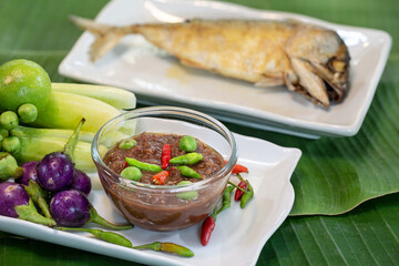 Thai Shrimp paste chili sauce (thai called  Nam Prik Kapi ) with fresh vegetables and fried steamed mackerel ripe, in white dish on green banana leaf
