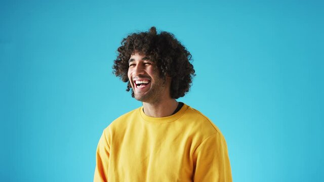 Studio portrait of confident smiling young man laughing against blue background - shot in slow motion