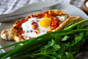 Selective focus. Macro. Khachapuri with egg and herbs on a plate.
