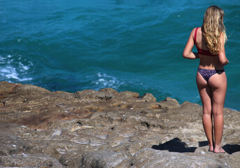 Young woman in a bikini standing on the rocks at Bronte Beach. She is looking out to the ocean