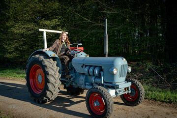 Junge Frau mit Spass an der Landwirtschaft sitzt auf einem Oldtimer - Traktor.