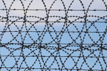 Fototapeta premium Barbed wire and razor wire wheels against a blue sky background