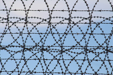 Barbed wire and razor wire wheels against a blue sky background