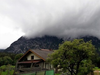 Old damaged, empty house in front of a mountain and a large white cloud 