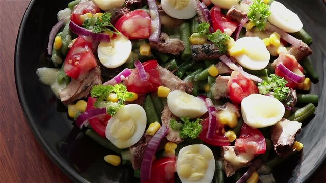 eat healthy tuna salad with boiled egg corn tomato red onion parsley green bean using fork close up