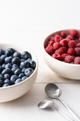 Raspberries and blueberries close-up in bowls on a white background, ripe juicy berries
