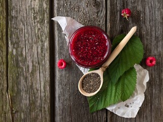 Raspberry jam with Chia seeds in a glass jar and a wooden spoon with Chia seeds on an old wooden background with space for text. Top view