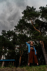 Young woman in full growth on background of pine trees and an approaching thunderstorm