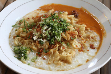 Bubur ayam or chicken porridge, Indonesian rice porridge with shredded chicken and chunks of cakwe. Breakfast dish of rice porridge with chicken, Chinese croissant, celery, and fried shallot