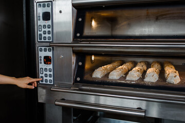 Close up baker's hand turn on the electric oven and for baking is the bread at baking manufacturer factory