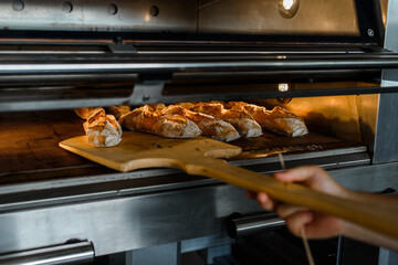 Close up of baker is taking off from oven the french baguette bread with wood peel at baking manufacture factory