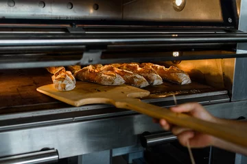 Foto op Plexiglas Close-up van de bakker vertrekt uit de oven, het franse stokbrood met houtschil in de bakfabriek © Med Photo Studio