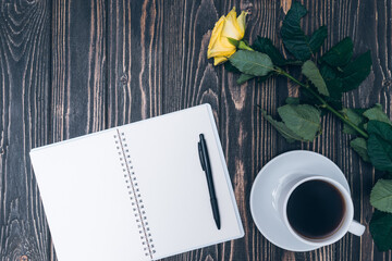 notebook, cup of coffee and yellow rose on wooden background. mock up