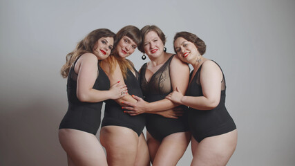 Group of happy oversize women in black bodysuits standing together over grey background