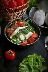 fresh mozzarella salad with lettuce and arugula leaves, pesto sauce, fresh cherry tomatoes and cedar nuts, on dark slate table background