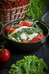 fresh mozzarella salad with lettuce and arugula leaves, pesto sauce, fresh cherry tomatoes and cedar nuts, on dark slate table background