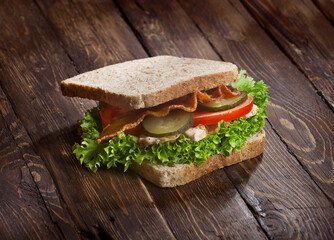 sandwich with smoked meat, green salad, fresh tomatoes and pickled cucumbers, on kitchen wooden table background