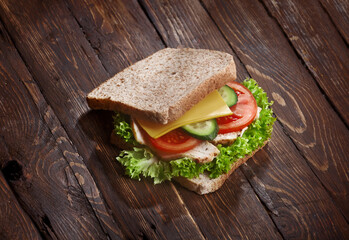 turkey sandwich closeup with fresh tomatoes, lettuce salad leaves, cucumber and cheese, on wooden rustic table background