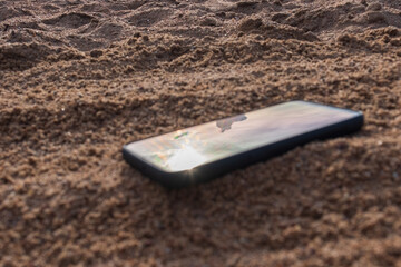 Mobile phone buried in the grey sand, lose your smartphone on the beach while on vacation.