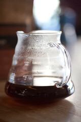 glass drip pot with black coffee on table, closeup with blurred background