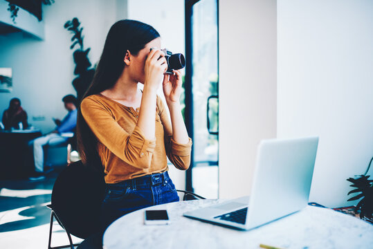 Professional female photographer taking photo on vintage camera for making illustrations in networks,skilled hipster girl fond of photography making picture and editing images on laptop computer