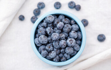 Blueberry or bilberry forest berries in blue ceramic plate on white tablecloth, top view