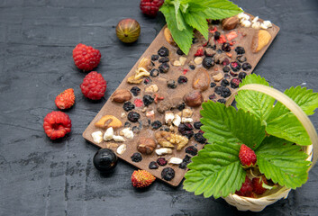 Chocolate bars, various ripe berries and mint leaves lie on a black slate background.