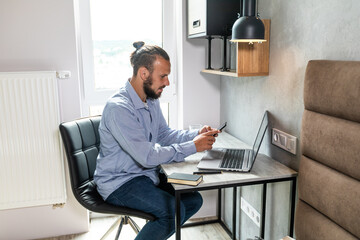 The guy sits at the computer, looks at the phone and replies to messages