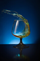 A splash of brandy in a cognac glass on a dark blue background with a reflection on the table.