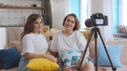 Obraz premium Two beautiful plus size girlfriends shooting video for internet blog sitting at home