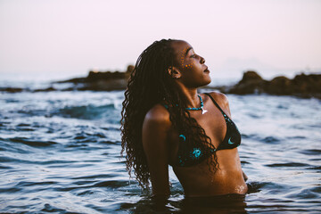 An elegant and beautiful young black woman in bikini in a beach in the sunset time  in summer. 